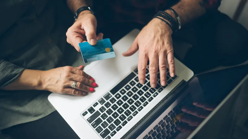 Two people at a laptop, one holding a payment card, reviewing account details online